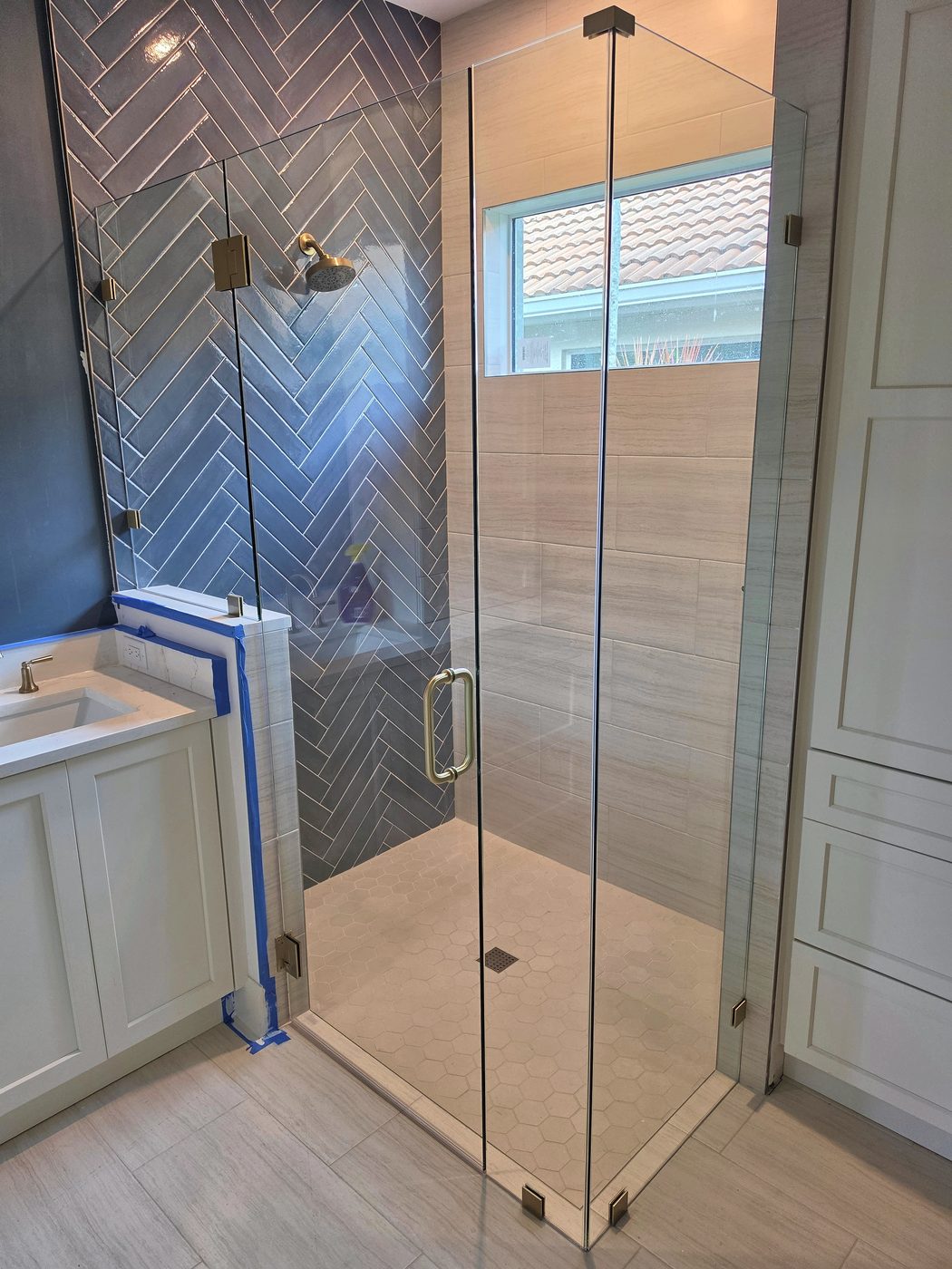frameless shower door with blue herringbone tile installed in Southwest Florida